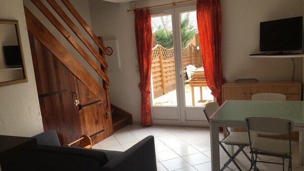 A room with a wooden staircase, a dining area with a table and chairs, a television mounted on the wall, and a sliding glass door leading to an outdoor area. - Semi-detached house close to the beach (Marseillan Plage)