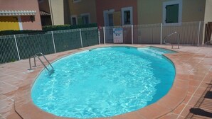 A swimming pool with a tiled deck, a metal fence, and a sign indicating it is a public pool. - Semi-detached house close to the beach (Marseillan Plage)