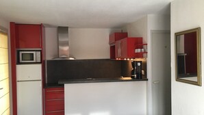 A compact kitchen with red cabinets, a microwave, and a coffee maker. - Semi-detached house close to the beach (Marseillan Plage)