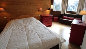 Une chambre à coucher aux murs lambrés, comprenant un lit, une commode, une table de chevet et une fenêtre avec des rideaux.