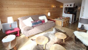 Un salon chaleureux avec un canapé, une petite table à manger et un coin cuisine à l’arrière-plan.