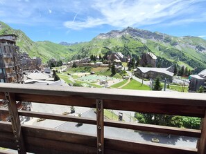 A mountain village with traditional buildings, a central square, and a view of the surrounding hills.