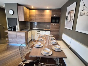 Una cocina moderna con área de comedor, que incluye una mesa de madera dispuesta para seis personas, una cafetera y un reloj en la pared.