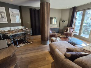 A modern living room with a sofa, a dining area with a table set for a meal, a large window with a view, and a tall column in the center. - Avoriaz: Wellness space, 8 pers, 90 sqm (Avoriaz)