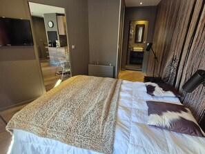 A modern hotel room with a large bed, a flat-screen TV, a desk, and a bathroom visible through an open door. - Avoriaz: Wellness space, 8 pers, 90 sqm (Avoriaz)