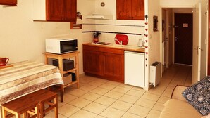 A compact kitchen with wooden cabinets, a microwave, a small refrigerator, and a dining area with a table and benches.