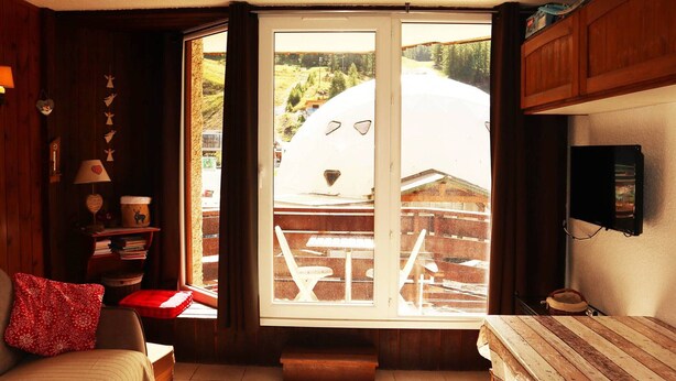 A cozy room with a large window, a bed, a wooden bench, and a small table.