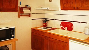A compact kitchen with wooden cabinets, a microwave, a sink, and a kettle.