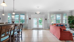 A spacious living room with a large window, a red sofa, and a dining area with wooden chairs and a bar.