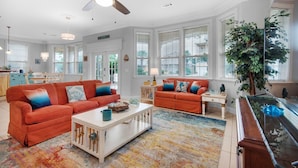 A spacious living room with two orange sofas, a white coffee table, and a large window with blinds.