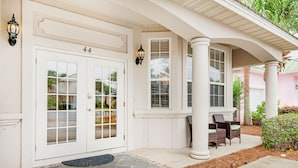 A house with a white exterior, a front door with glass panels, and a porch with wicker furniture.