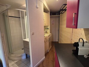 Une cuisine compacte avec une douche, des placards en bois et une machine à café.
