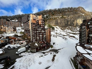 Een besneewd berglandschap met moderne gebouwen, waaronder een meerlaags hotel met balkons en een skigebied.