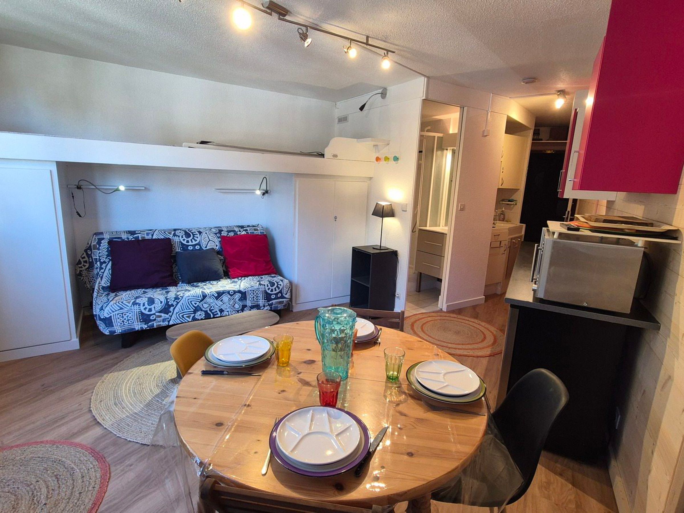 A compact living space with a dining area, kitchenette, and a sofa with patterned cushions.