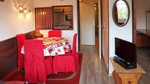 A room with a dining table set for two, a television on a wooden stand, and a mirror on the wall. - Luxury studio 4 pers, ski-in/ski-out, fireplace, balcony, no pets, free wifi (Les Orres)