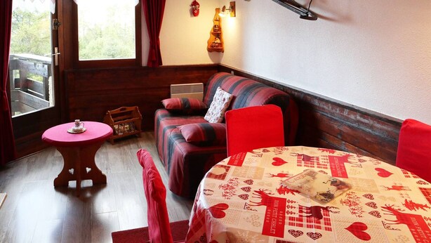 A cozy room with a sofa, a small table, and a chair. There is a window with curtains, a wall-mounted rack, and a decorative item. - Luxury studio 4 pers, ski-in/ski-out, fireplace, balcony, no pets, free wifi (Les Orres)