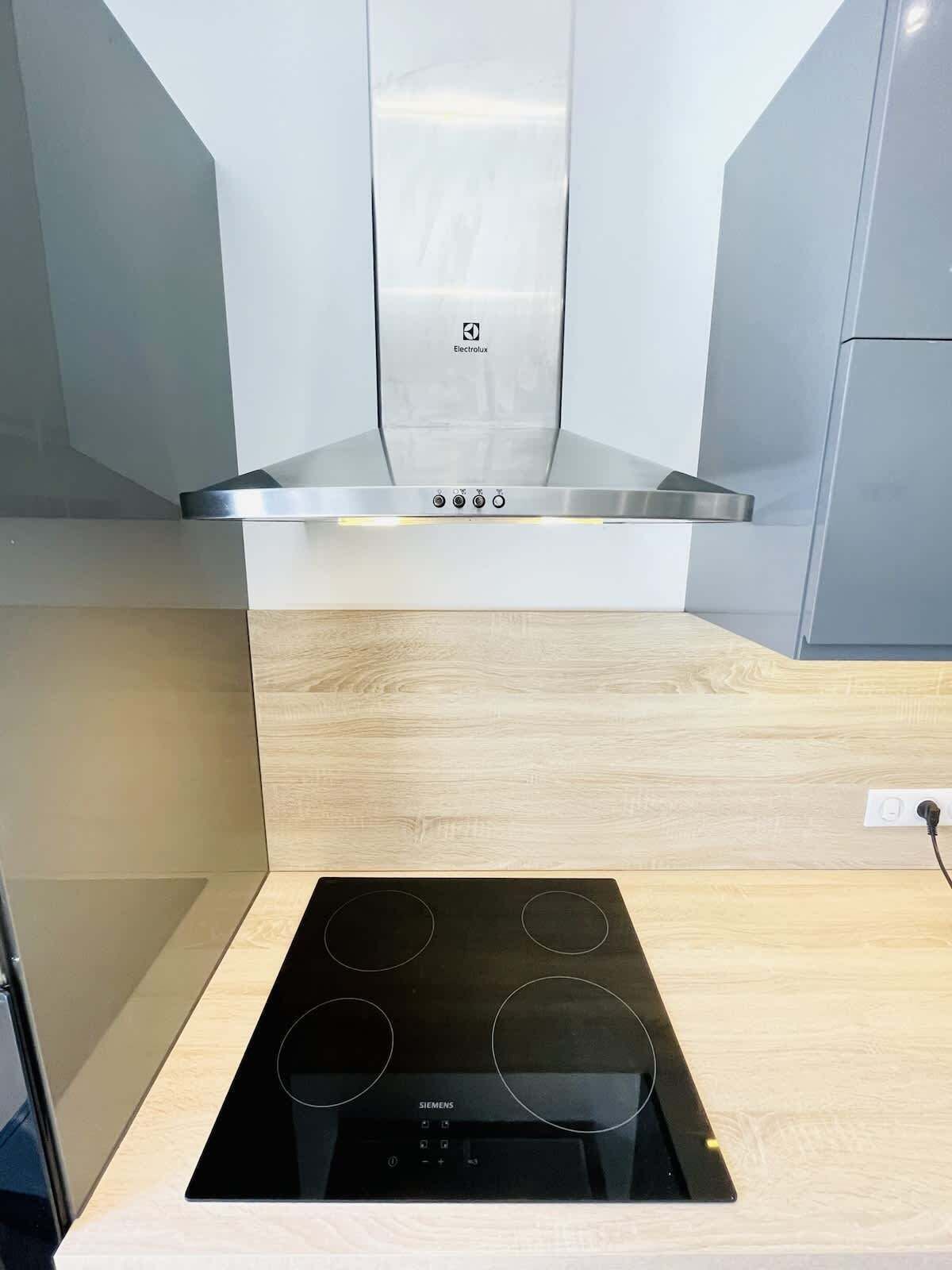 Een keuken met een roestvrijstalen afzuigkap, een zwart inductiekookplaat en een licht houten aanrecht.