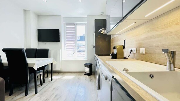 A modern kitchen with a built-in oven, a sink, and a dining area with a table and chairs. - Romy Schneider (Vittel)
