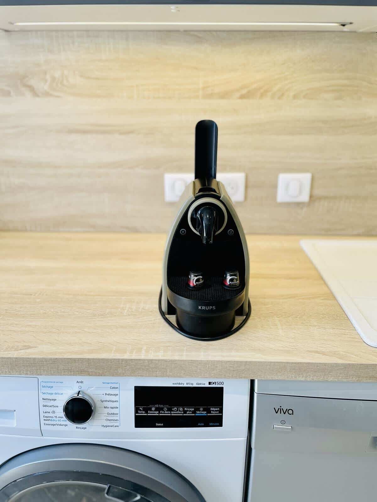 Una lavadora compacta con panel de control y un electrodoméstico pequeño y negro de pie sobre una encimera de madera.