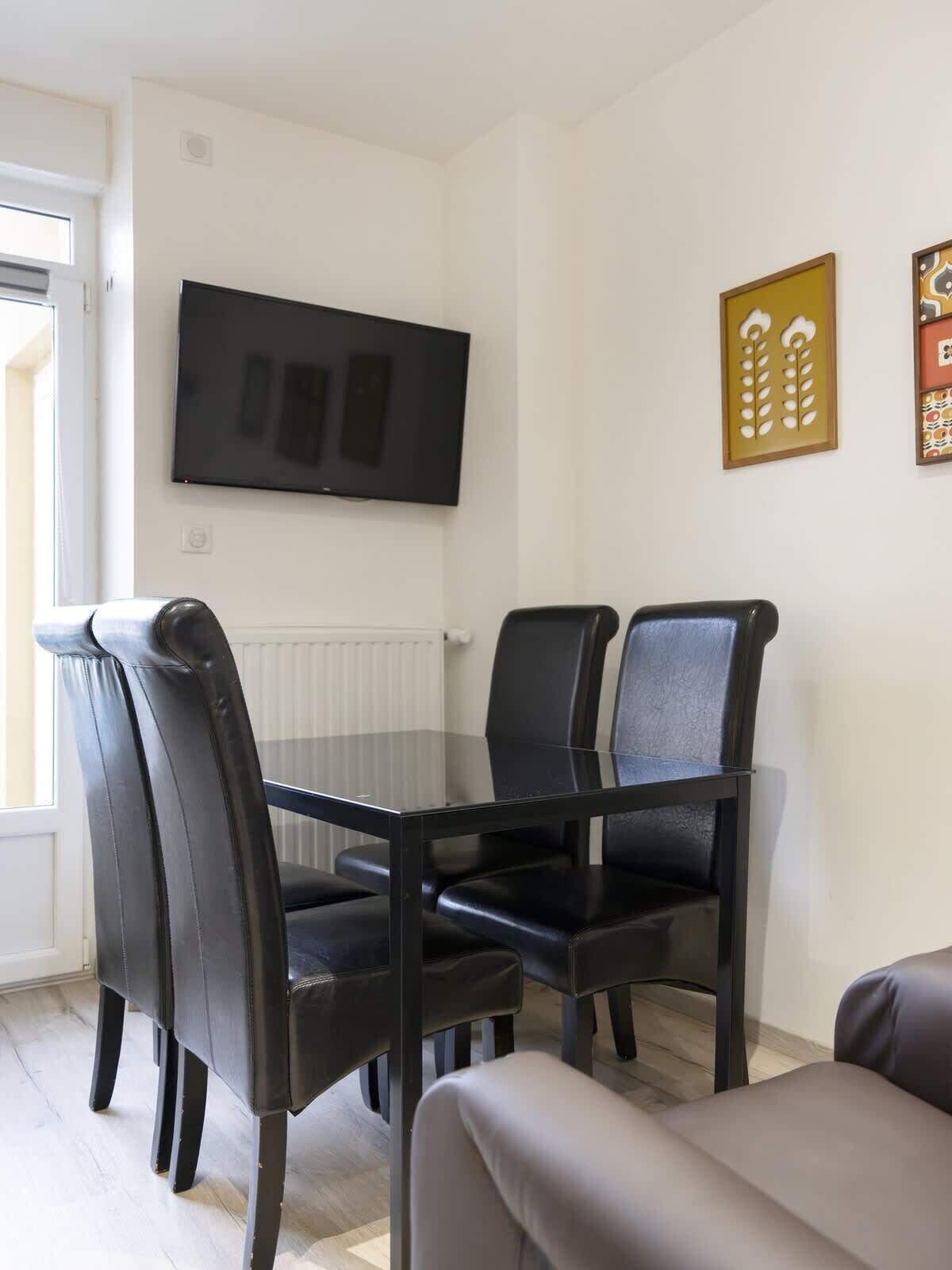 A dining area with a table and chairs, a television mounted on the wall, and decorative wall art.