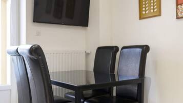 A dining area with a table and chairs, a television mounted on the wall, and decorative wall art.
