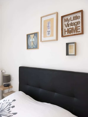 A bedroom with a black headboard, a bed with a white and gray patterned bedspread, and three framed wall art pieces.
