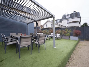 A patio with a table and chairs, a covered area, and a well-maintained lawn.