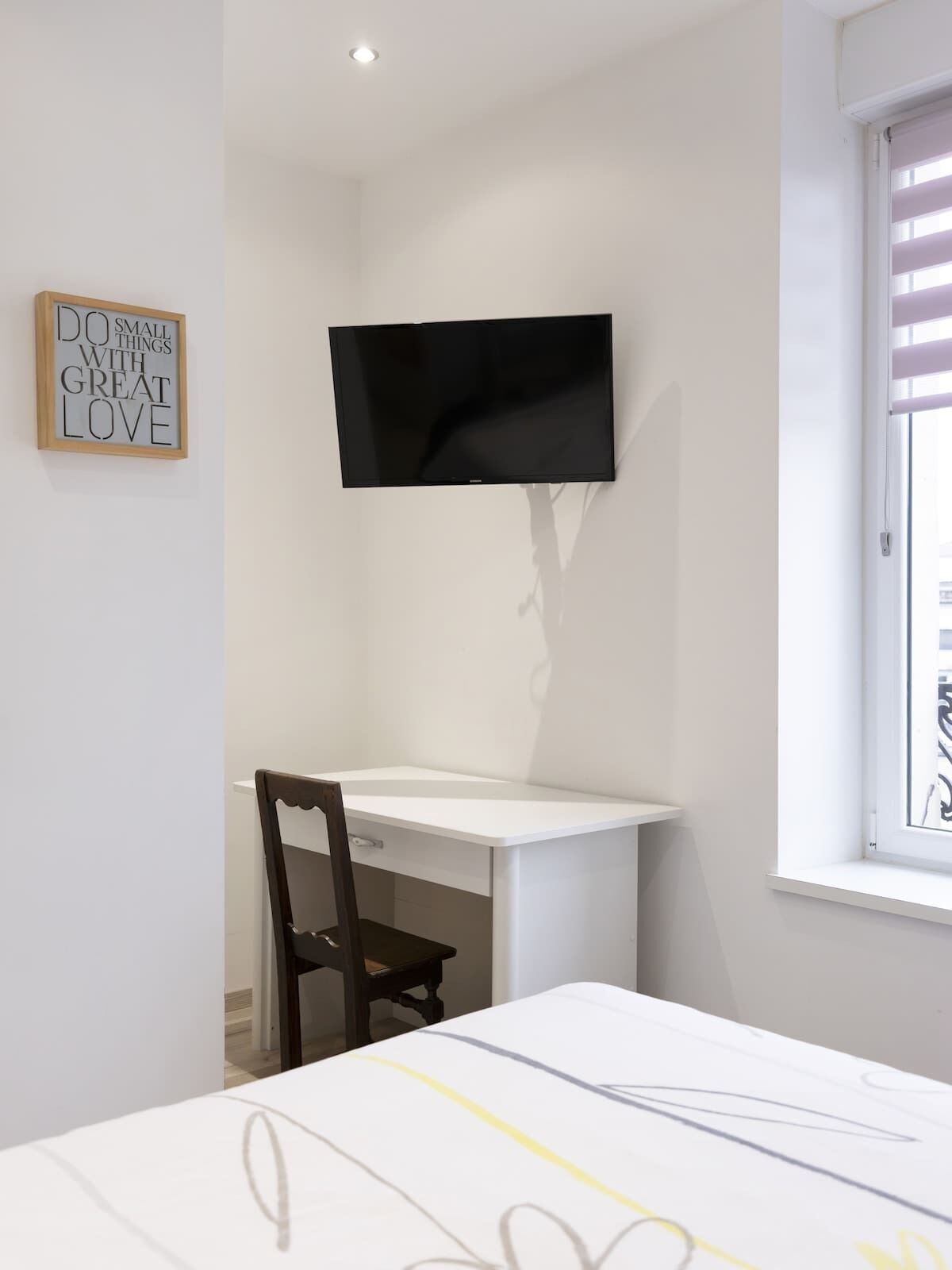 Une pièce comprenant un lit, un bureau, une chaise, un téléviseur fixé au mur et une fenêtre.