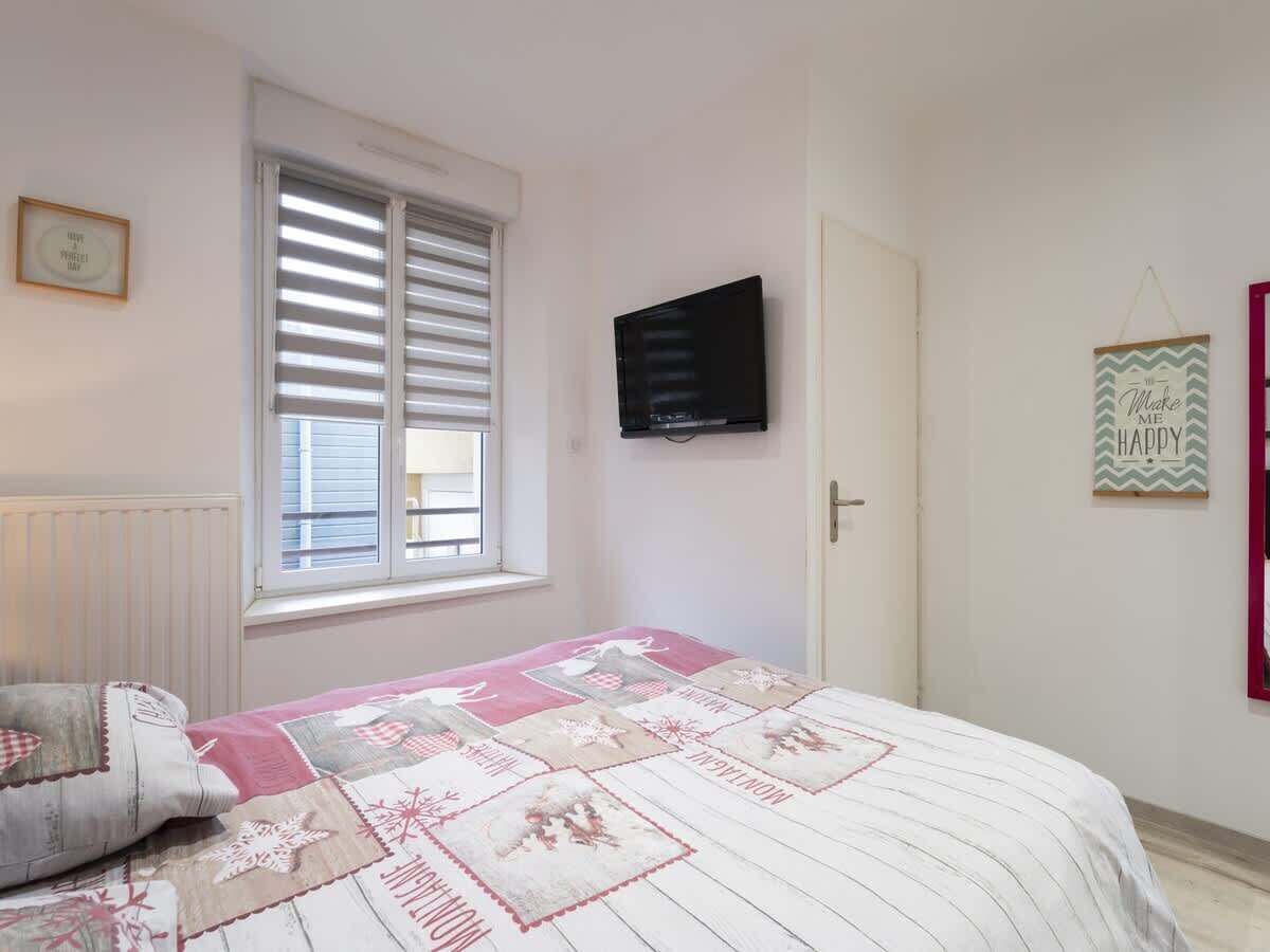 A bedroom with a bed, a window with blinds, a television mounted on the wall, and a door.