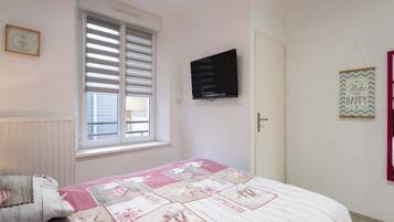 A bedroom with a bed, a window with blinds, a television mounted on the wall, and a door.