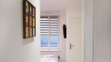 Une chambre à coucher avec un lit, une fenêtre avec des stores, une porte et une œuvre d’art accrochée au mur.