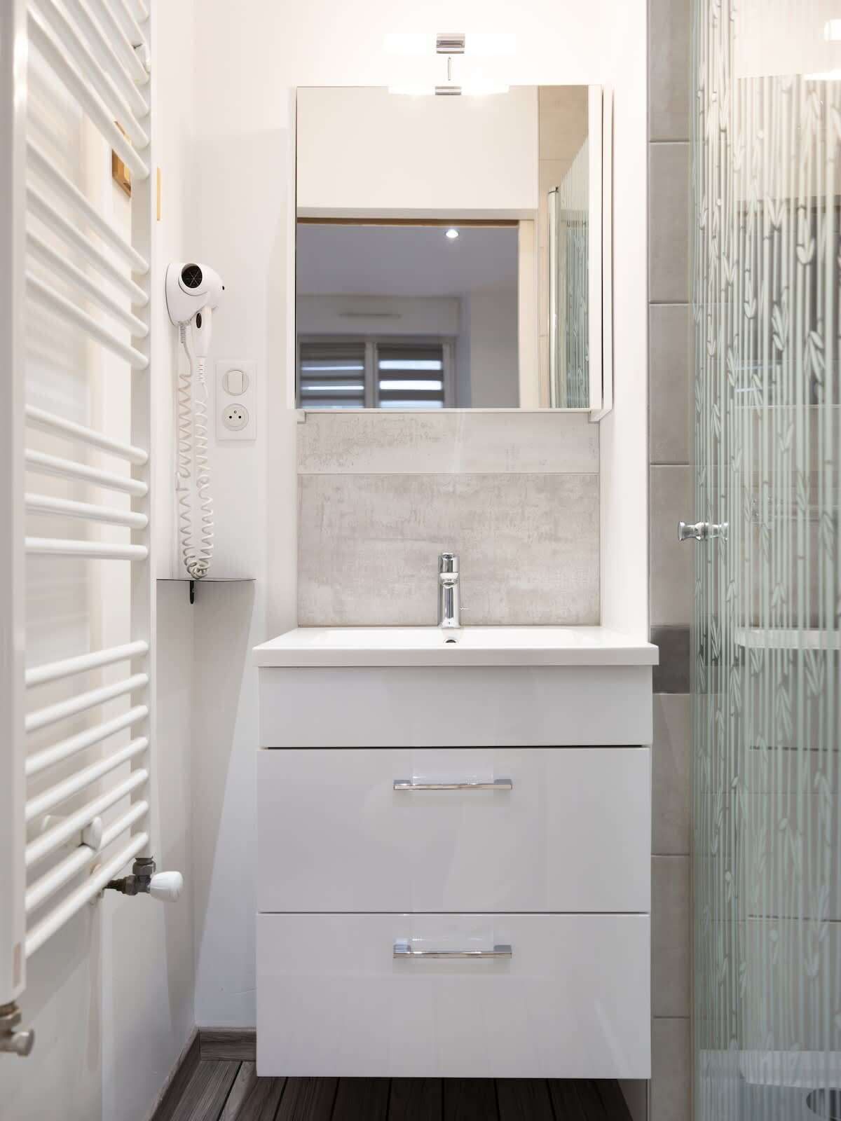 Une salle de bain avec un meuble-lavabo blanc, un miroir, un lavabo et une cabine de douche.