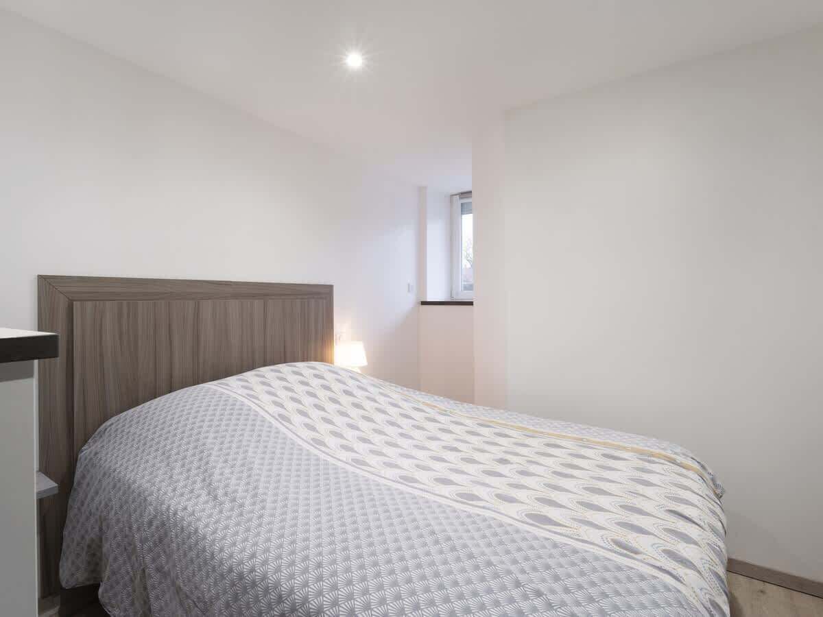 Een slaapkamer met een bed, nachtkastje, raam en plafondlamp.