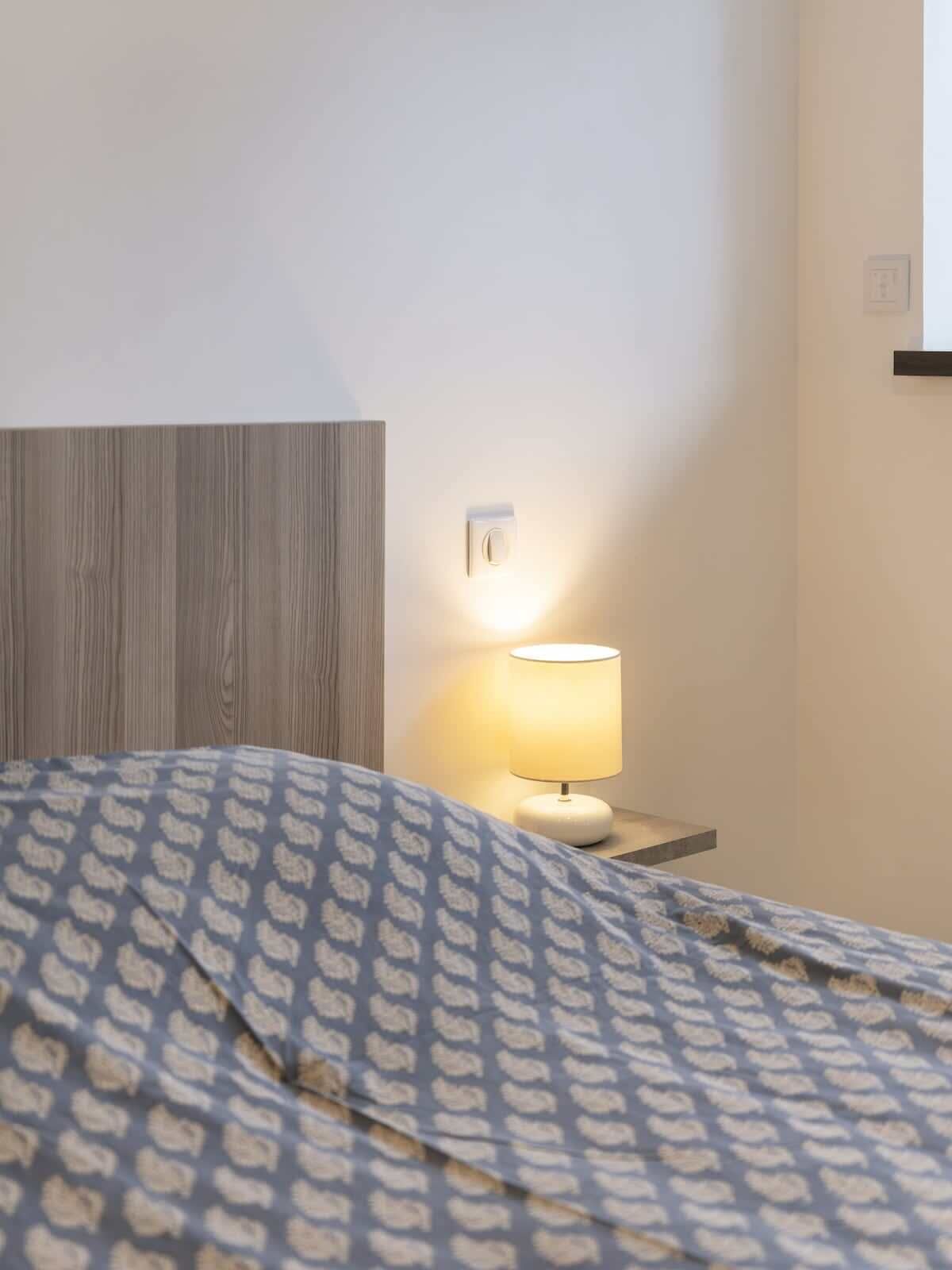 A hotel room with a bed, a nightstand with a lamp, and a wooden headboard.