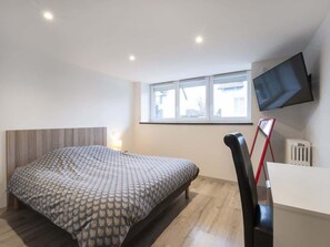 A bedroom with a bed, a desk, a chair, a TV, and a window.