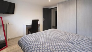 A bedroom with a bed, a desk, a chair, a TV mounted on the wall, and a wardrobe. - Jade (Vittel)
