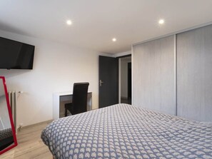 A bedroom with a bed, a desk, a chair, a TV mounted on the wall, and a wardrobe. - Jade (Vittel)
