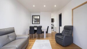 Un salon moderne avec un canapé gris, un fauteuil inclinable gris, une table à manger avec des chaises et un tapis blanc.