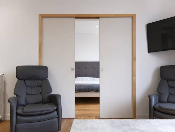 A room with a bed, two chairs, a TV, and a sliding closet door.
