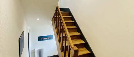 Een trap met houten treden en een houten leuning, die leidt naar een plateau met een radiator en een ingelijst schilderij aan de muur.