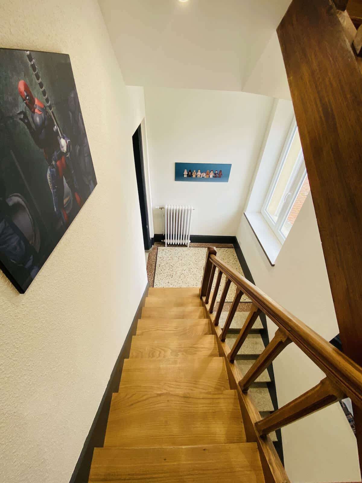 Eine Holztreppe mit Geländer, einem Heizkörper und einem an der Wand befestigten Kunstwerk.