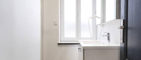 A modern bathroom with a white vanity, a large window, and a dark door.