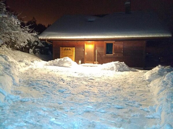 A wooden cabin with a snow-covered roof and a lit entrance.