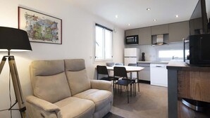 A modern living room with a sofa, a dining table with chairs, a kitchen area with a microwave, and a TV. - Chalet de Romy (Vittel)