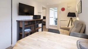 A modern living room with a flat-screen TV, a dining table, a sofa, and a lamp. - Chalet de Romy (Vittel)