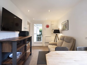 A modern living room with a flat-screen TV, a sofa, a dining table, and a lamp. - Chalet de Romy (Vittel)