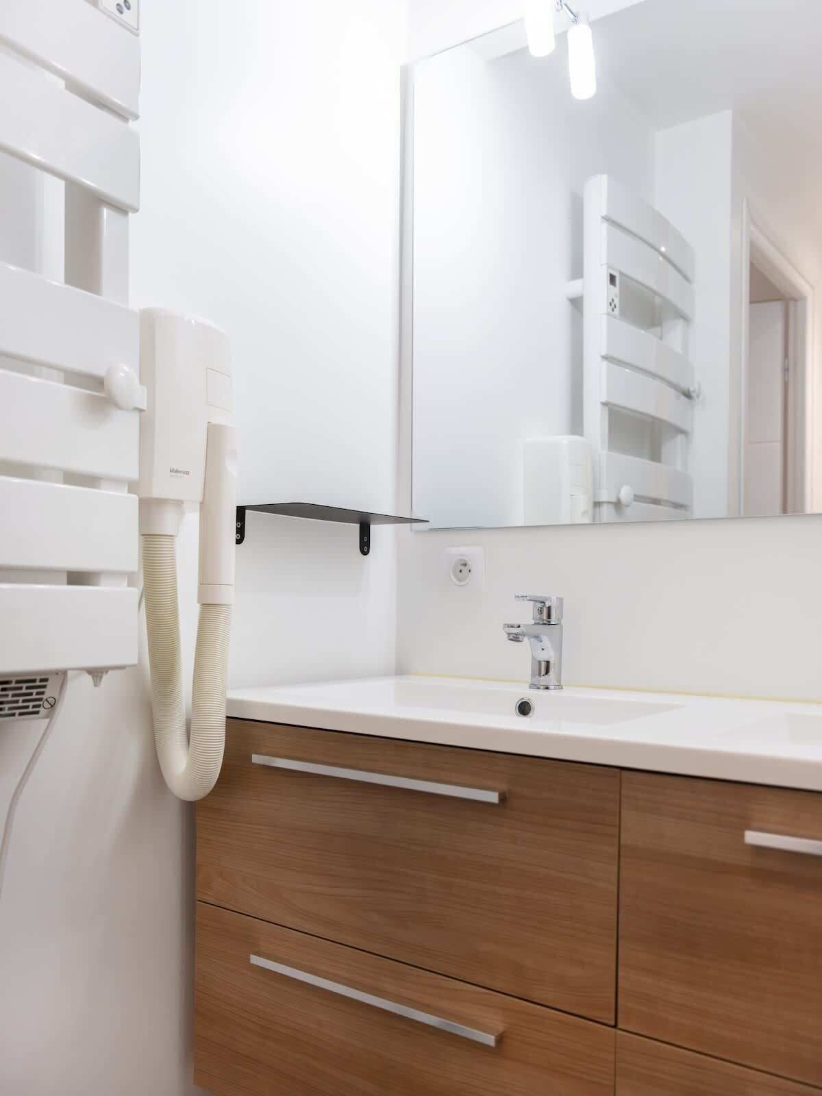 Ein modernes Badezimmer mit einem weißen Waschbecken, Holzschränken, einem Spiegel und einem Fön.