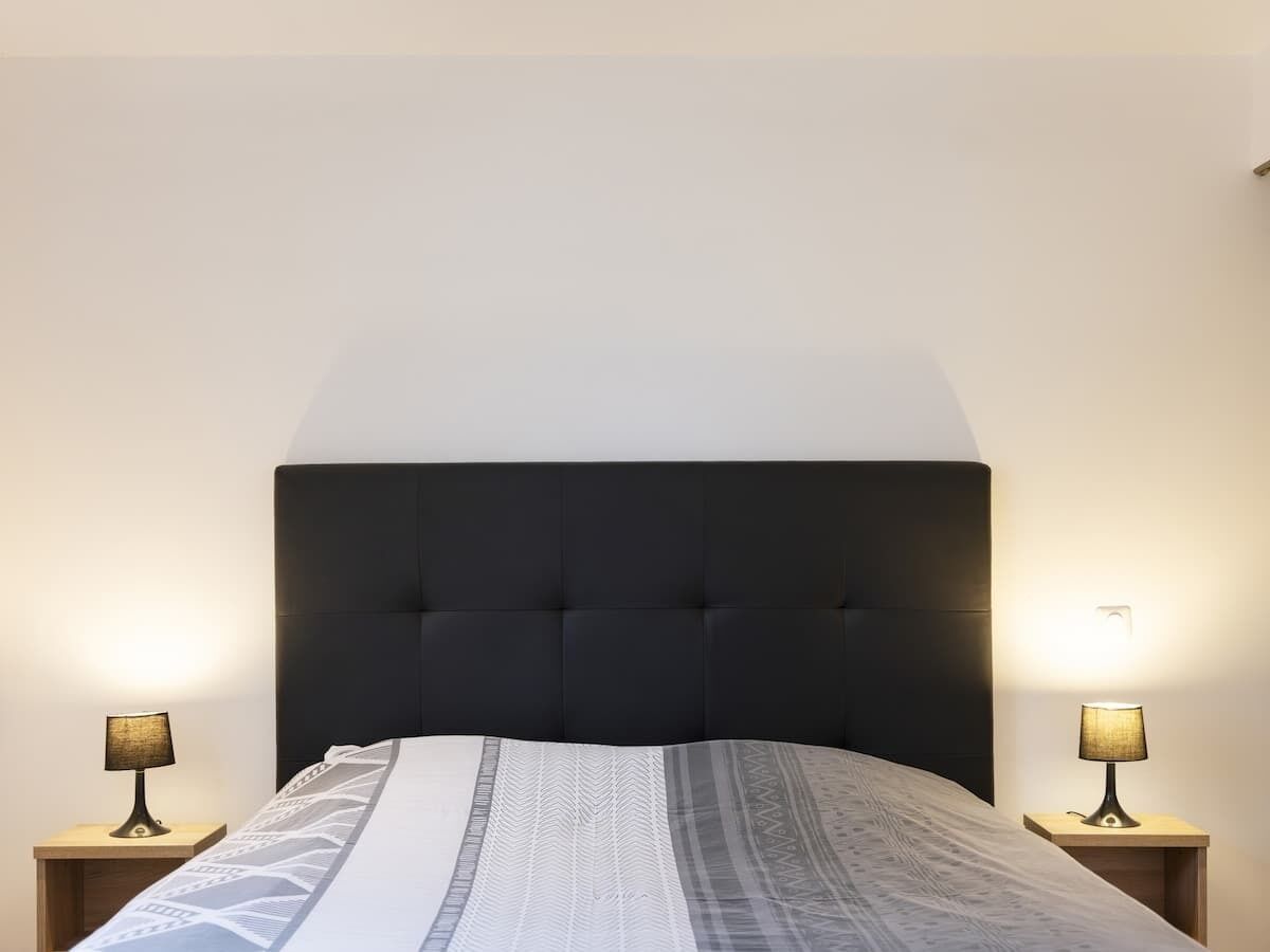 A bed with a dark headboard, two bedside lamps, and a patterned bedspread.