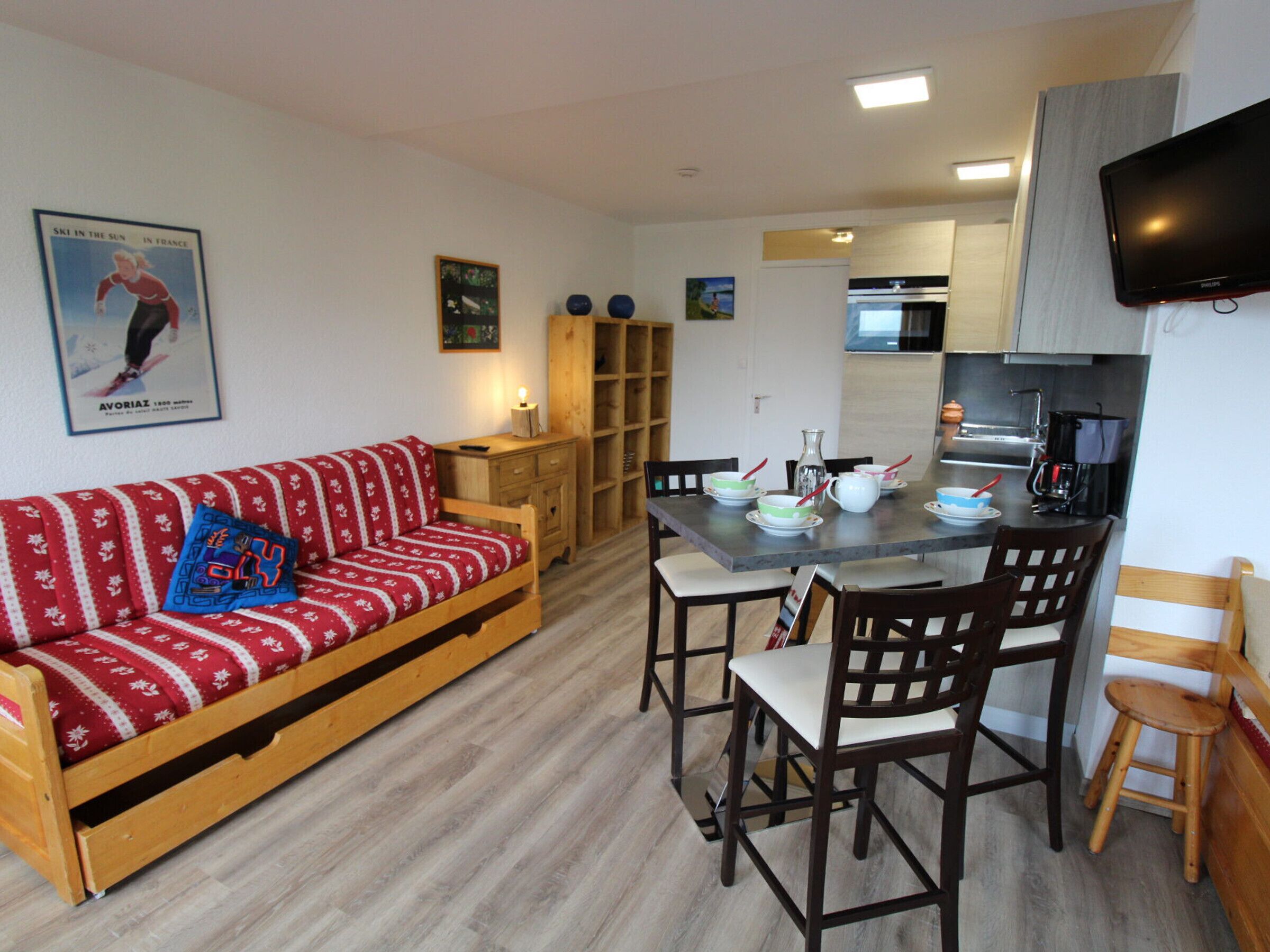 A compact living space with a sofa, dining table, chairs, a TV, and a kitchenette.