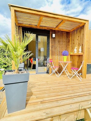 A wooden deck with a small table and chairs, a potted plant, and a building entrance with a glass door.